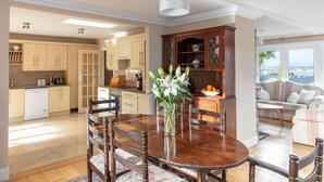 A spacious kitchen with wooden cabinets, a dining table with chairs, and a view to the living area. - Bay View Cottage 3 bedroom house VRBO (County Kerry)
