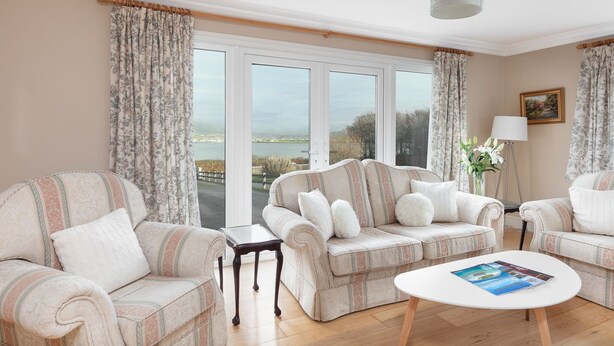 A living room with two sofas, a coffee table, and a view of the sea through large windows. - Bay View Cottage 3 bedroom house VRBO (County Kerry)