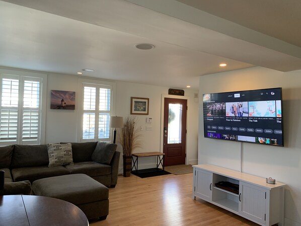 Una sala de estar con sofá, una mesa de centro, televisor montado en la pared y una puerta que da a otra habitación.