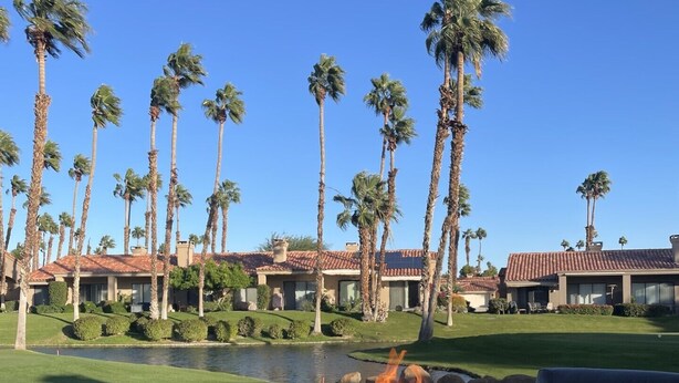 A fire feature in a circular planter, a pool, and a view of a resort with palm trees and buildings. - Palm Valley Getaway with all the amenities & golf water view! (Palm Desert)