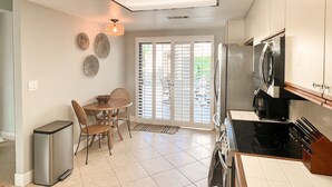 A compact kitchen with a dining area, a trash bin, and a large window with blinds. - Palm Valley Getaway with all the amenities & golf water view! (Palm Desert)
