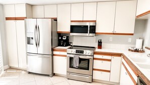 A modern kitchen with white cabinets, stainless steel appliances, and a tiled floor. - Palm Valley Getaway with all the amenities & golf water view! (Palm Desert)