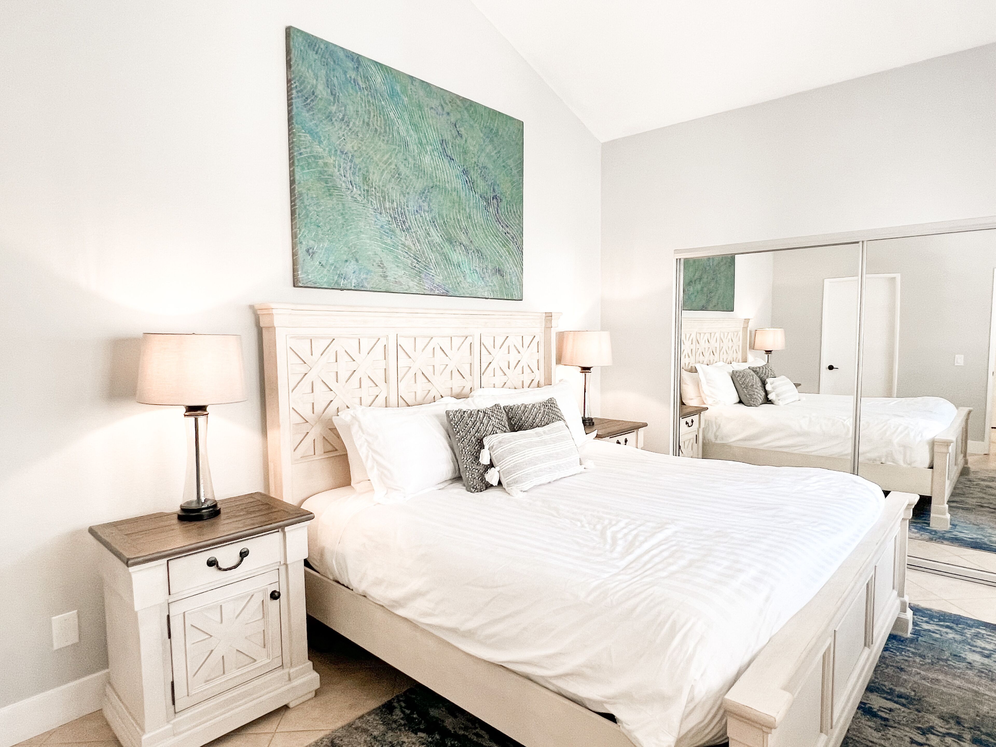Habitación de hotel con una cama grande, dos mesitas de noche, un espejo y un cuadro en la pared.