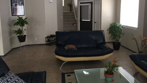 A living room with a black leather sofa, a glass coffee table, and potted plants. - Enjoy your stay in a clean, safe environment easy access to freeways (Las Vegas)