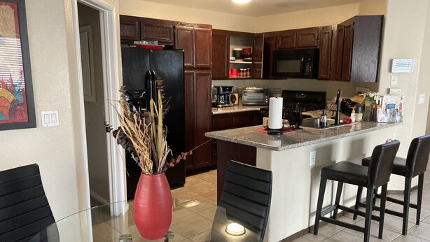 A modern kitchen with dark wooden cabinets, a stainless steel refrigerator, a microwave, and a central island with bar stools. - Enjoy your stay in a clean, safe environment easy access to freeways (Las Vegas)