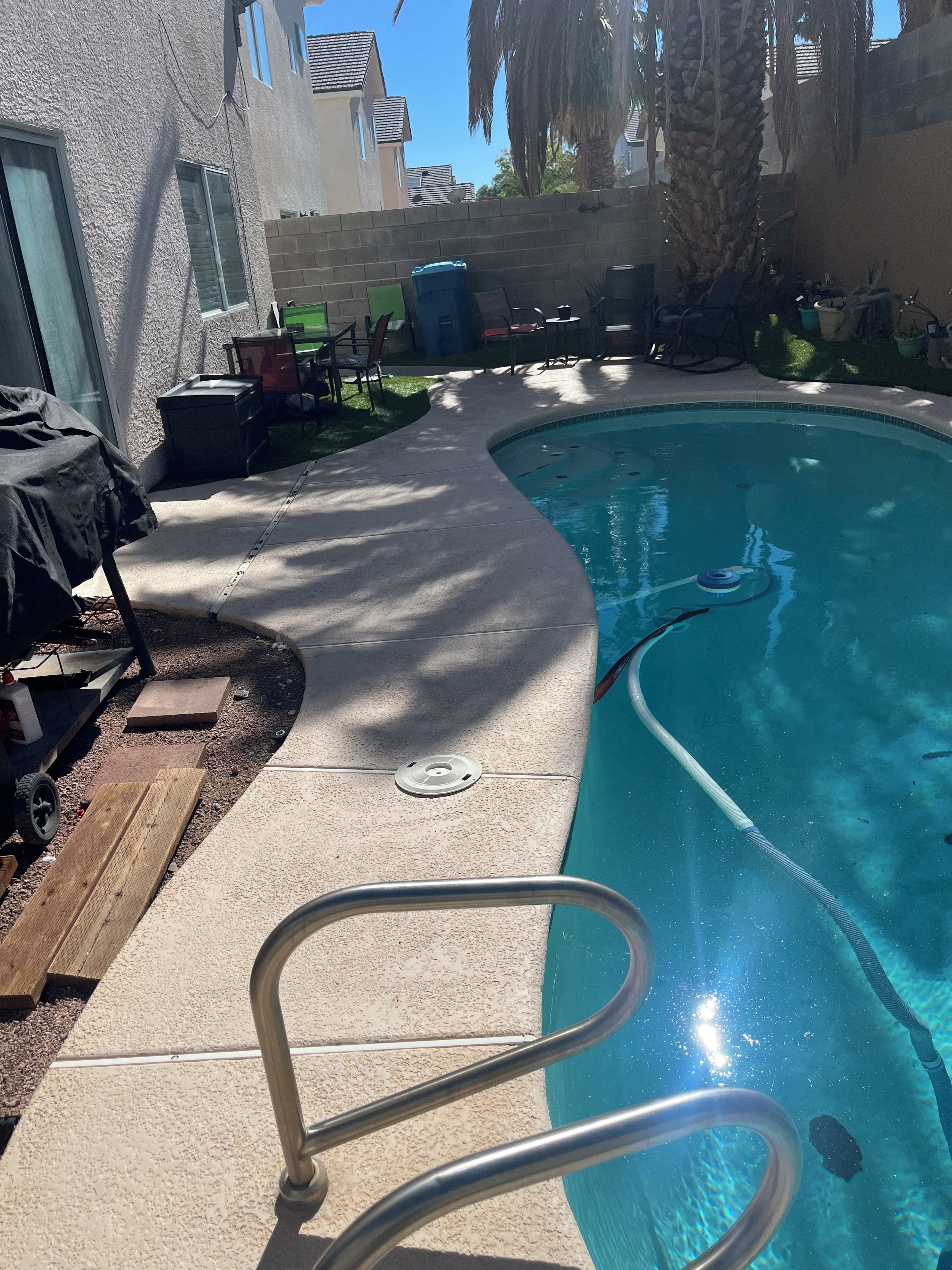 Une piscine avec un escalier en métal, entourée de meubles de jardin et d’un palmier.