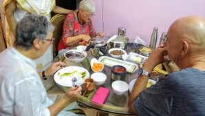 Un grup de persones assegudes al voltant d'una taula plena de plats i recipients diversos.