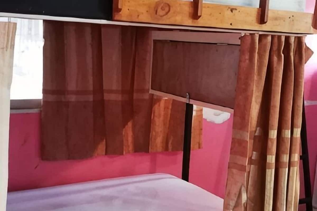 A room with a bed, a wooden headboard, a window with curtains, and a wall with a partial view of another room.