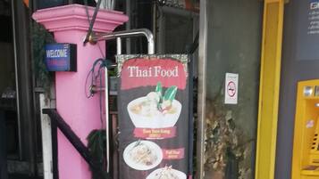 A Thai food restaurant entrance with a pink wall, a welcome sign, and a menu board displaying various dishes.