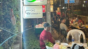 An outdoor dining area with tables, chairs, and people eating. There are signs for an EV charger and a hostel named 'OK HOME'. - OKHOME HOSTEL (Bang Phli)