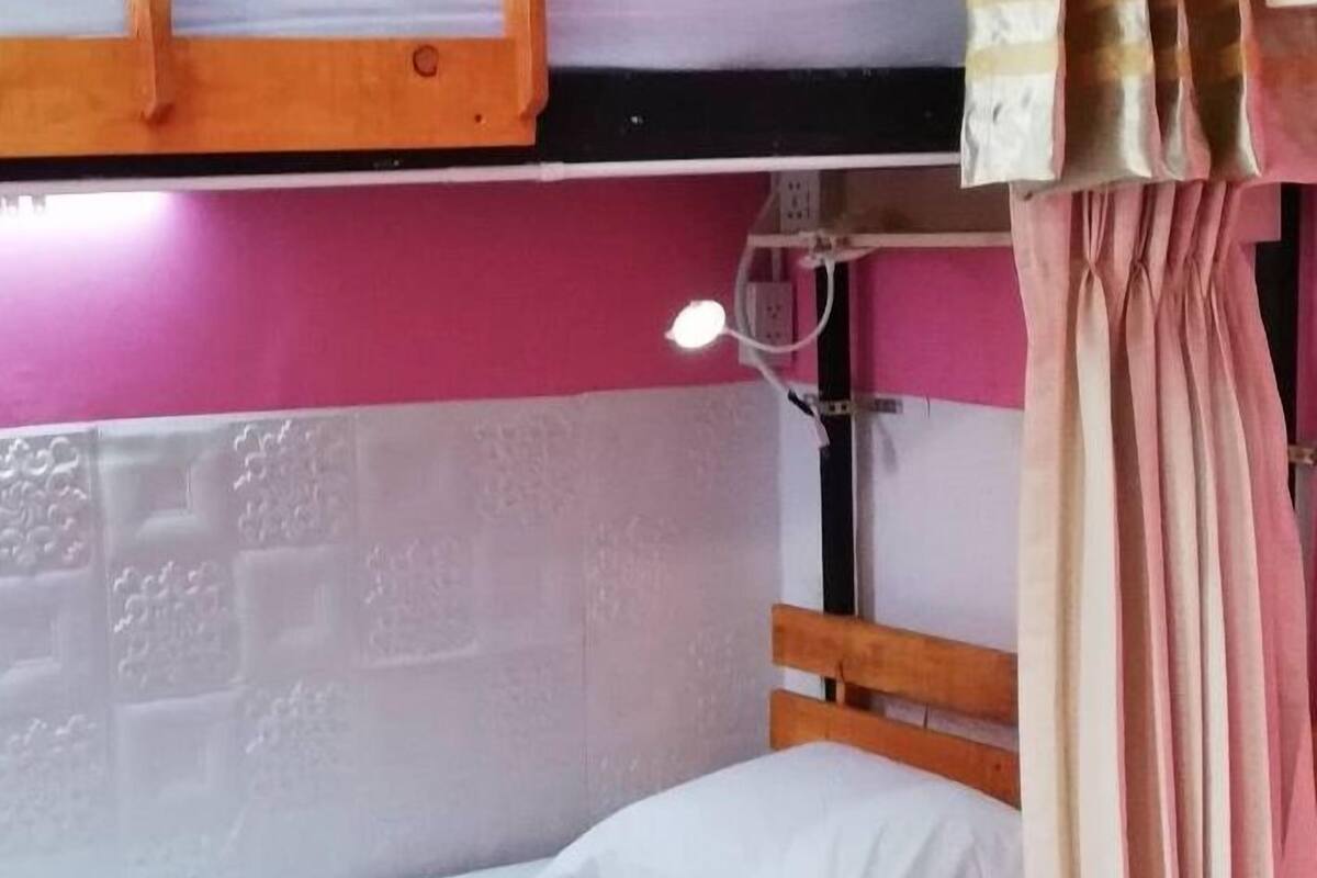 A bunk bed room with a wooden frame, a white mattress, and a pink wall.
