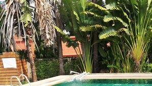 A clear blue pool with tiled edges, surrounded by palm trees and a wooden deck. - OKHOME HOSTEL (Bang Phli)