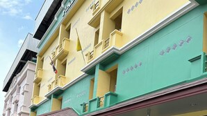 A multi-story hotel with a green and yellow facade, a vending machine, and a small garden area. - OKHOME HOSTEL (Bang Phli)