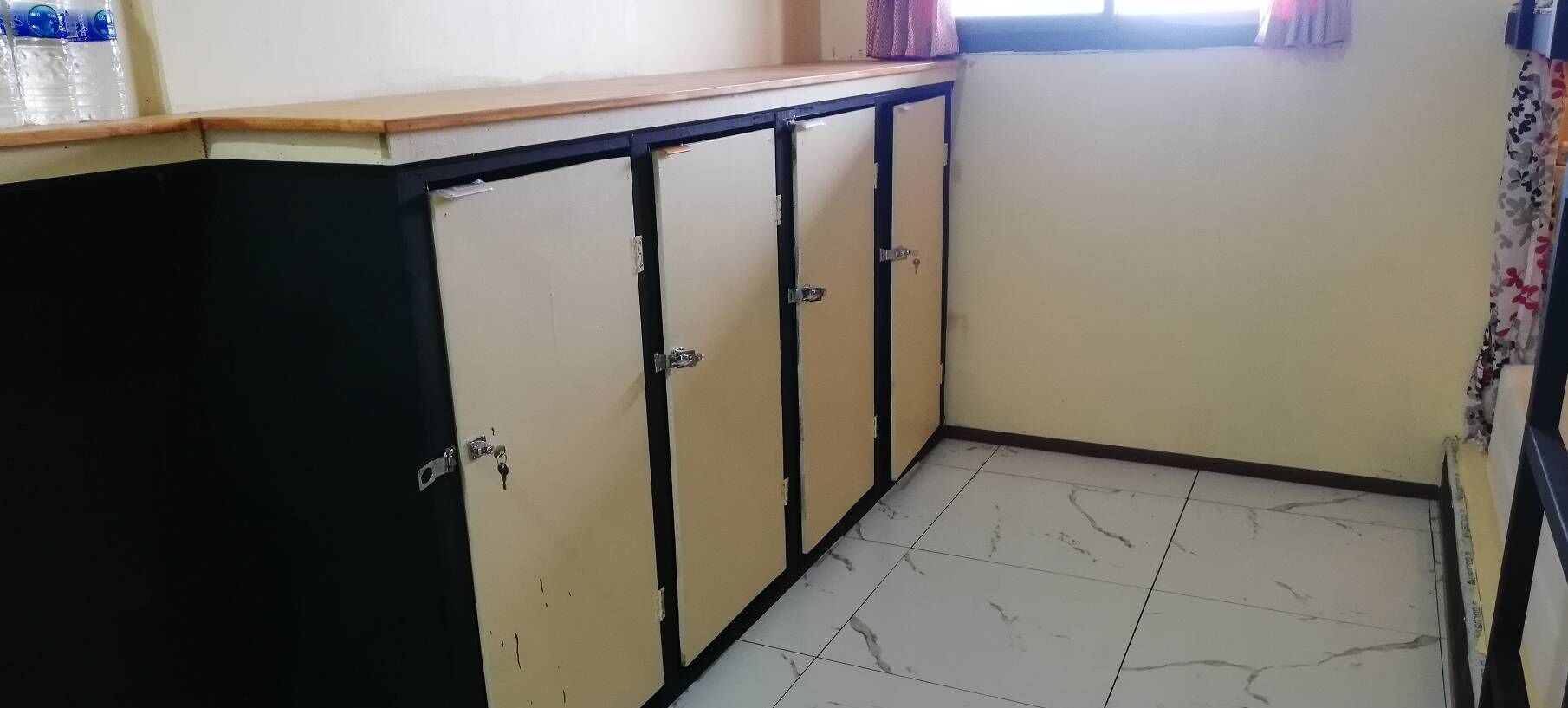 A small kitchen with a black and beige cabinet, a tiled floor, and a window with curtains.