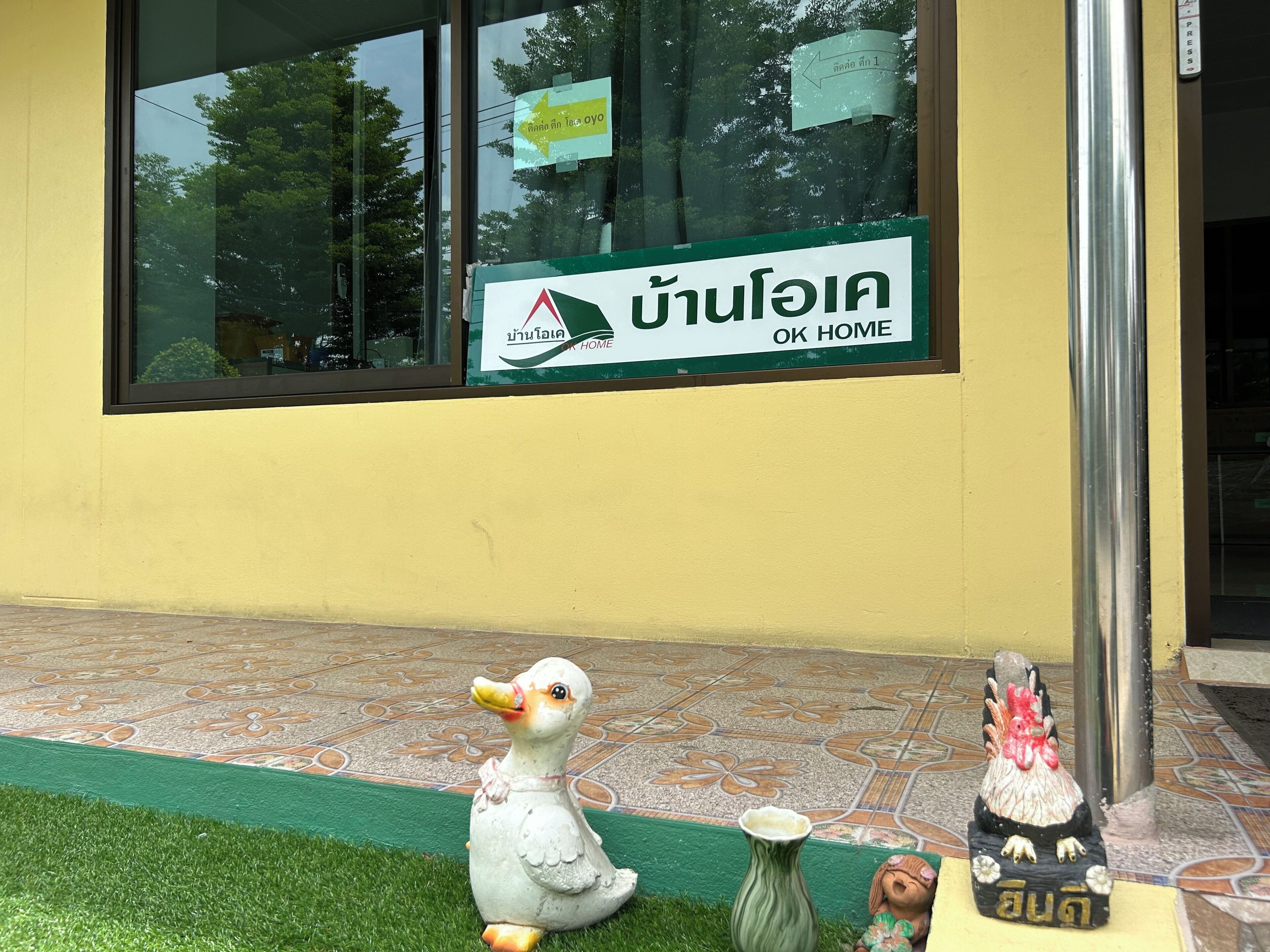 A building with a sign that reads 'OK HOME' and a small duck decoration on the ground.