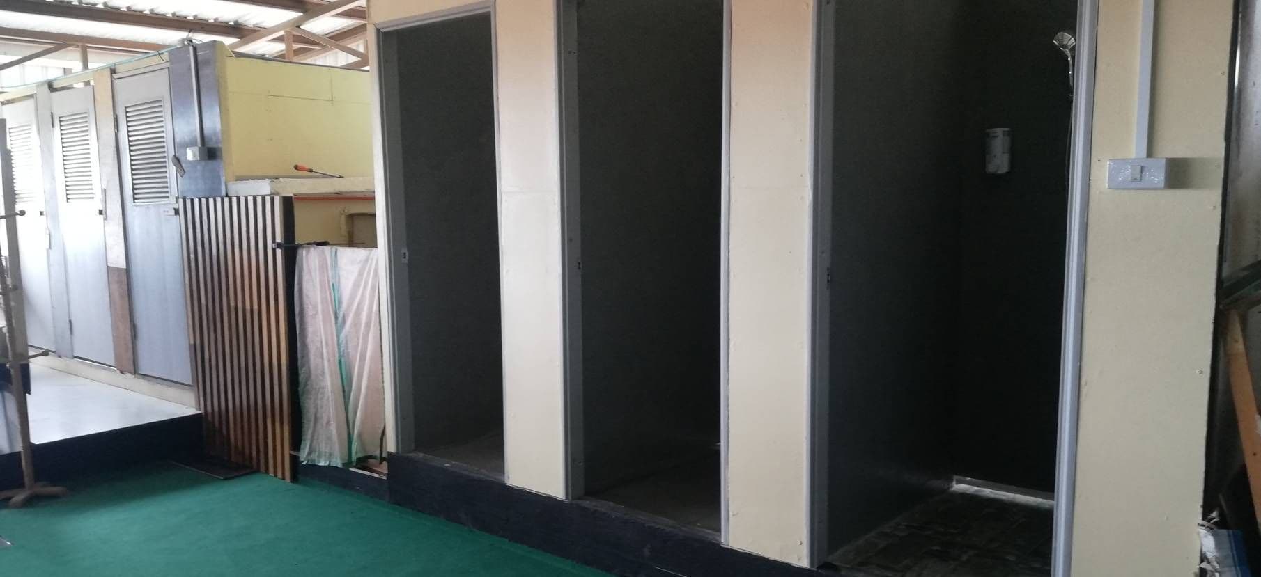 Un pasillo con varias puertas, algunas con ventanas persianas, y un suelo cubierto de moqueta verde.