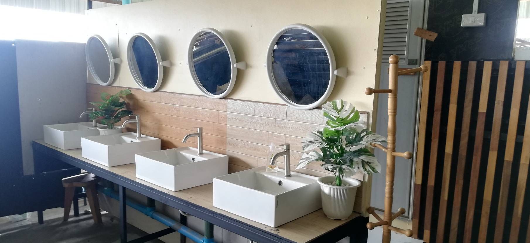 Une salle de bain avec quatre lavabos, chacun étant surmonté d’un miroir. Des plantes en pot sont disposées sur le comptoir.