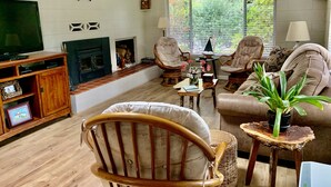 A living room with a fireplace, comfortable seating, a television, and a large window with a view of trees.