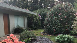 A garden with pink and orange flowers, a stone pathway, and a building with a brown door.