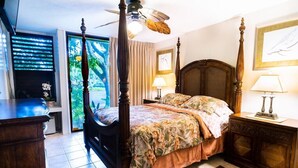 Ein Schlafzimmer mit Himmelbett, Deckenventilator und Blick auf einen Garten durch eine Schiebetür.