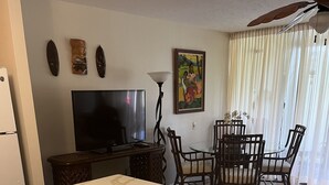 Eine Küche mit Marmorarbeitsplatte, Holzschränken, einem Essbereich mit Glastisch und Stühlen, einem Fernseher und Wanddekoration.