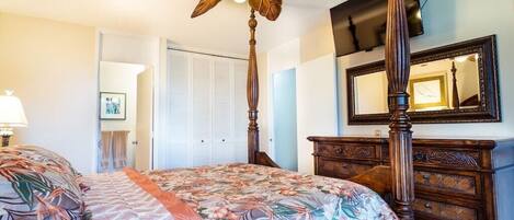 Een slaapkamer met een hemelbed, een plafondventilator, een dressoir en een spiegel.