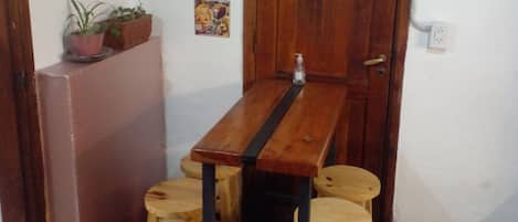 Una habitación pequeña con una mesa de madera y cuatro taburetes, una puerta con un letrero y diversas decoraciones en las paredes.