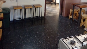 A kitchen with a stove, stools, a wooden shelf, a trash bin, and a wall clock. - Hostel Piltri  (El Bolson)