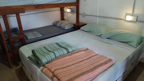 A bunk bed room with two lower beds and a top bunk. There are bedside lamps, a power outlet, and a wall-mounted light switch. - Hostel Piltri  (El Bolson)