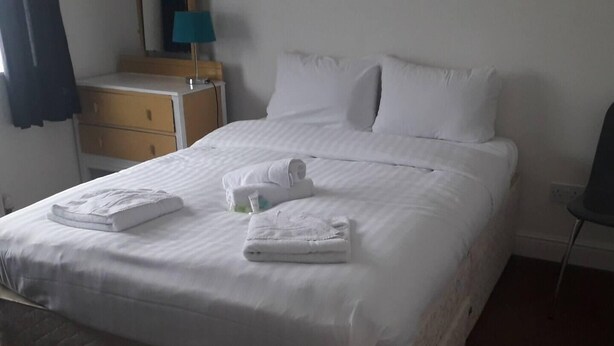 Un letto rifatto con lenzuola e asciugamani bianchi, un comodino in legno con una lampada e una sedia in una camera d'albergo.