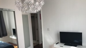 Une chambre à coucher avec un lit, un téléviseur posé sur un meuble, un miroir et un luminaire blanc fixé au plafond.
