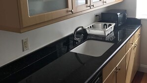 Une cuisine avec un plan de travail noir, des armoires de couleur beige et une fenêtre équipée de stores.