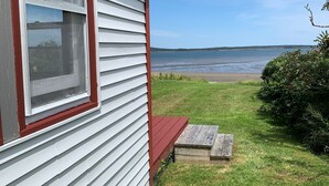 A house with a red front door, a window with a view of the beach, and a grassy yard. - Cozy cottage, steps from the beach. (Lubec)