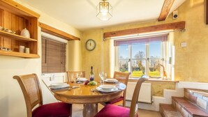 A dining area with a round wooden table, red upholstered chairs, and a window with a view of the outdoors. - Church Cottage (CA), Castle Acre, Norfolk (Castle Acre)