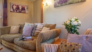 A cozy living room with a brown sofa, striped pillows, a magazine, and a vase of flowers. - Church Cottage (CA), Castle Acre, Norfolk (Castle Acre)