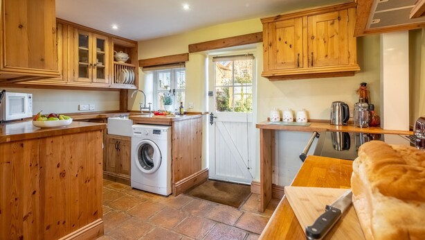 A kitchen with wooden cabinets, a washing machine, a cutting board, and a knife. - Church Cottage (CA), Castle Acre, Norfolk (Castle Acre)