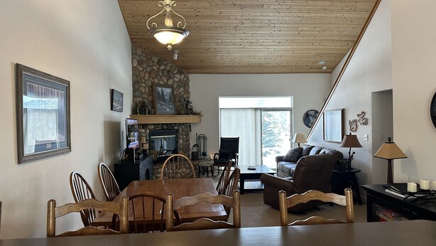 En hyggelig stue med en stenspir og træloft, samt et spiseområde med bord og stole.