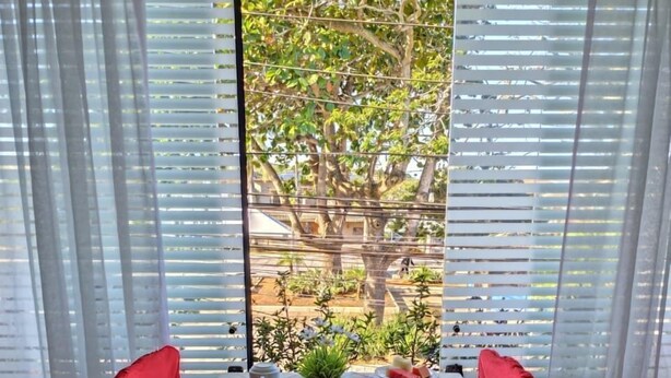 A dining table with a variety of food items and drinks, set against a backdrop of a tree and a window with blinds. - Pousada Capua (Búzios)