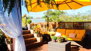 An outdoor patio with wicker furniture, potted plants, and a yellow umbrella. - Pousada Capua (Búzios)