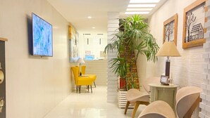 A hotel lobby with a reception desk, yellow chairs, a large potted plant, and artwork on the walls. - Pousada Capua (Búzios)