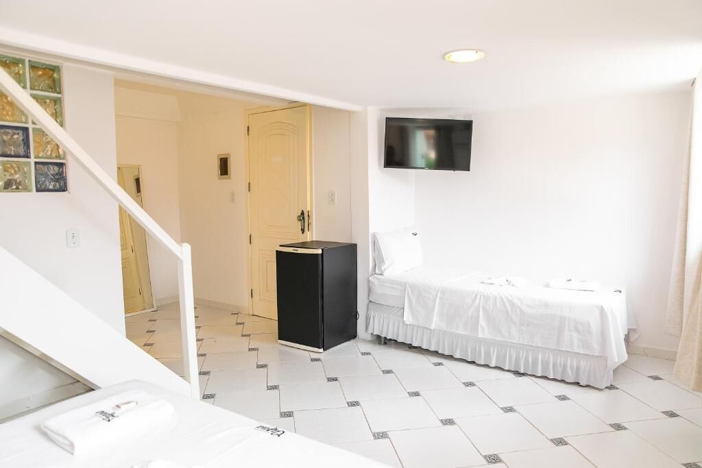 Habitació d'hotel amb un llit, un televisor fixat a la paret i un petit armari negre.