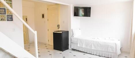 Habitació d'hotel amb un llit, un televisor fixat a la paret i un petit armari negre.