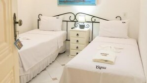 A bedroom with two beds, a nightstand, a painting, and a ceiling fan. - Pousada Capua (Búzios)