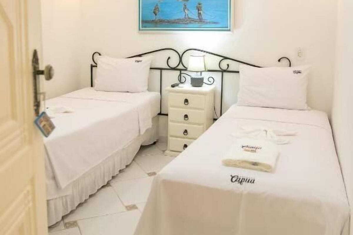 Quarto com duas camas, uma mesinha de cabeceira, um quadro e um ventilador de teto.
