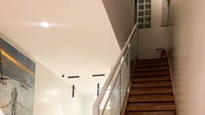 A staircase with wooden steps and a glass railing, leading to a landing with a white wall and a painting. - Pousada Capua (Búzios)