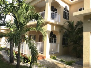 Un edificio de varios pisos con balcones, una palmera y un camino de grava.