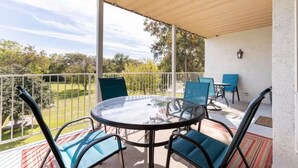 Un espacio al aire libre techado con una mesa redonda y sillas, una barandilla y vistas a un paisaje verde.