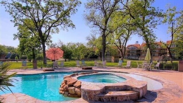 Una piscina con un jacuzzi, rodeada de baldosas de piedra y mobiliario de exterior.
