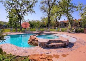 Une piscine avec un jacuzzi, entourée de carreaux de pierre et de mobilier d’extérieur.