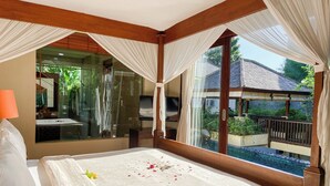 A bedroom with a large bed, a TV, and a view of a pool and outdoor area. - Alea Villa (Ungasan)